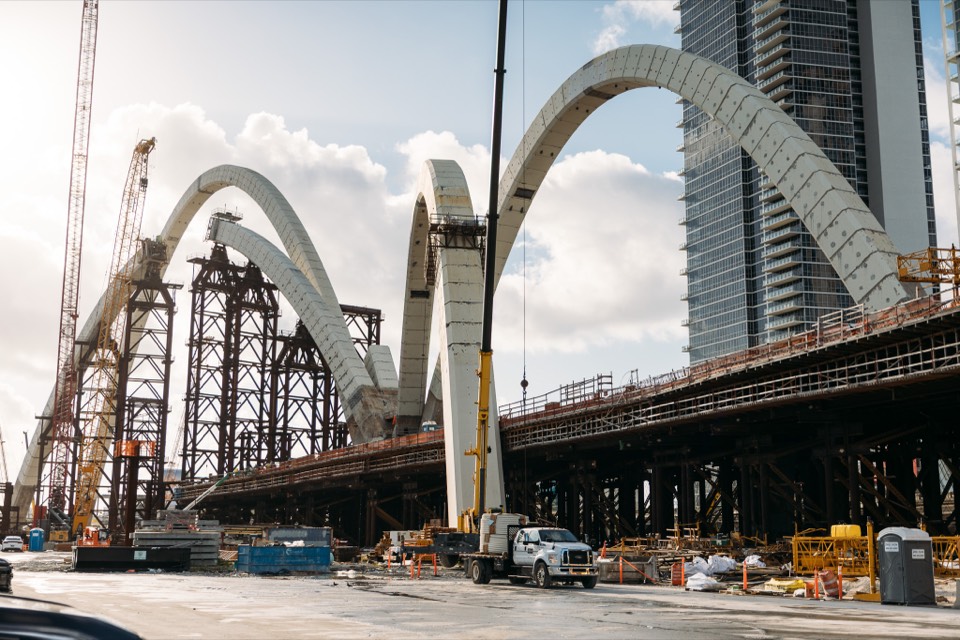 Massive white arches of an Ardurra bridge project under construction with cranes against a tower
