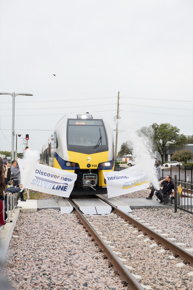 A Silver Line train breaking through a ribbon banner at its launch celebration